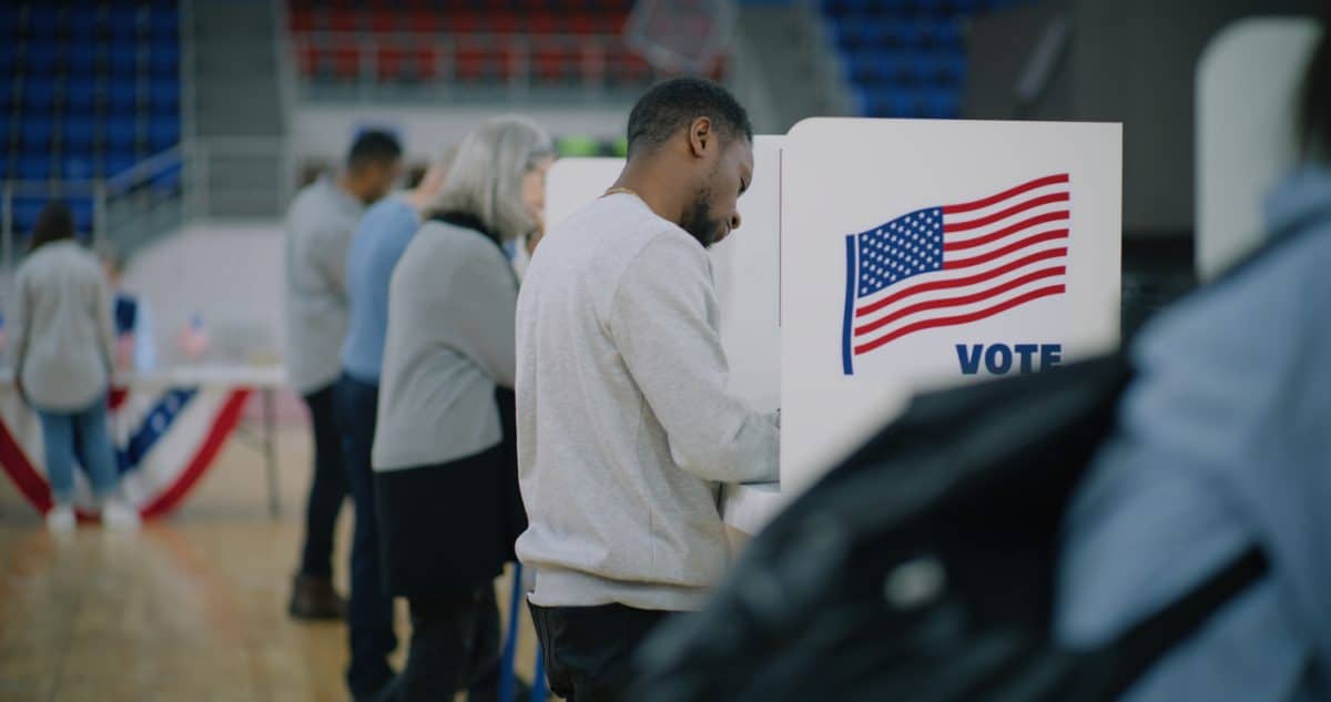 Elderly male voter with bulletin in hands comes to voting booth. Photo Multicultural American citizens come to vote in polling station.