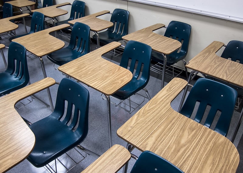 Eleven school desks, the kind with attached chairs, closely spaced in three rows. No one is in the chairs.